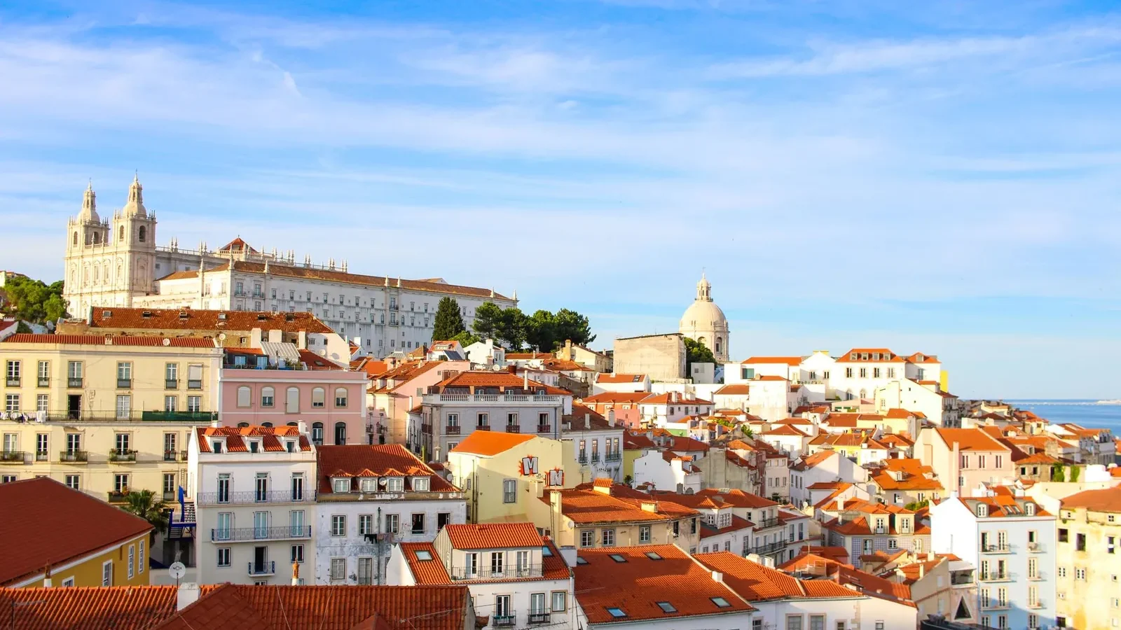 Lisbon waterfront on a clear May morning, with trams and outdoor café tables along the Tagus River