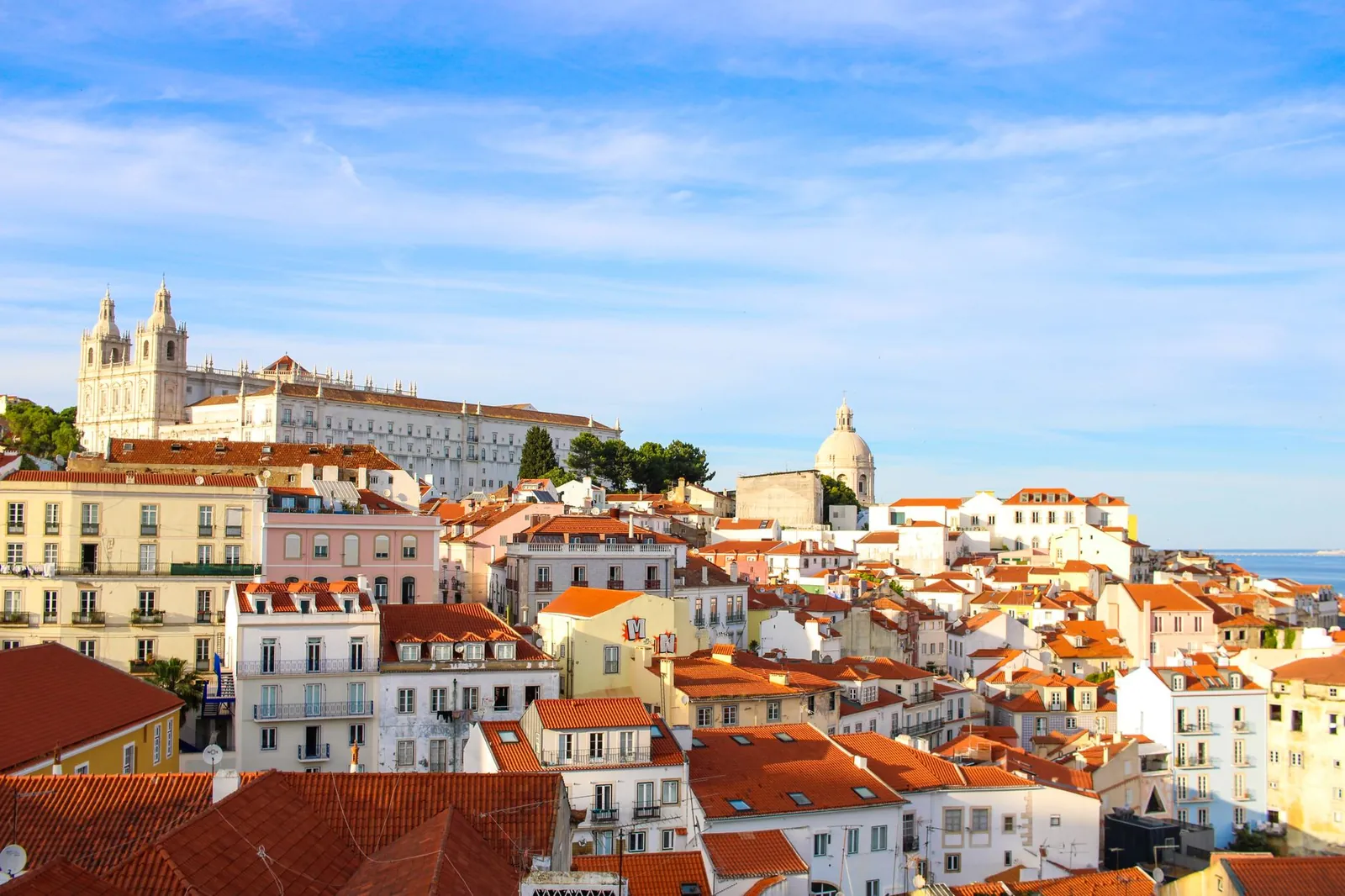 Lisbon waterfront on a clear May morning, with trams and outdoor café tables along the Tagus River