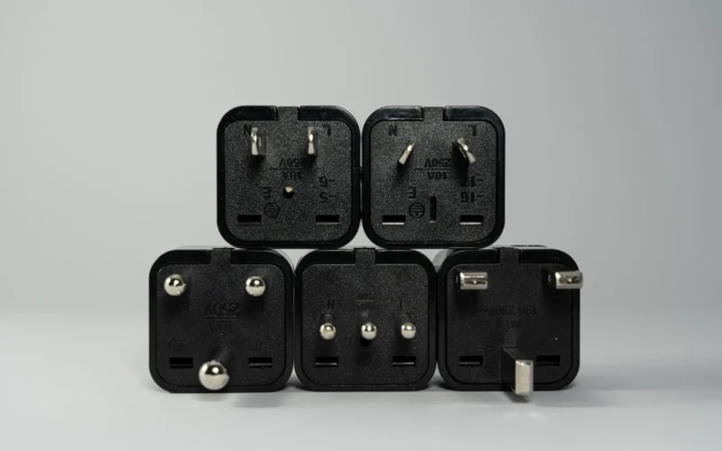 Six travel adapters arranged on a white surface showing Type C, G, I and universal plug configurations with USB ports visible