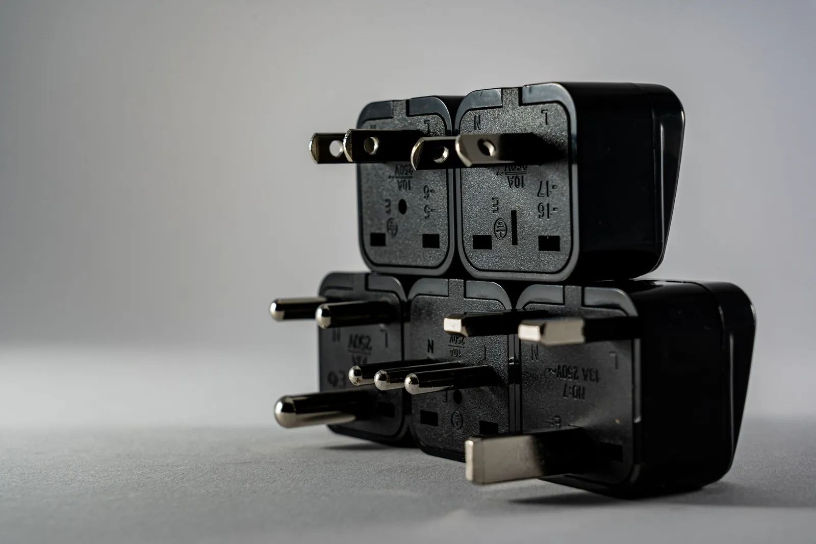Six travel adapters arranged on a white surface showing Type C, G, I and universal plug configurations with USB ports visible