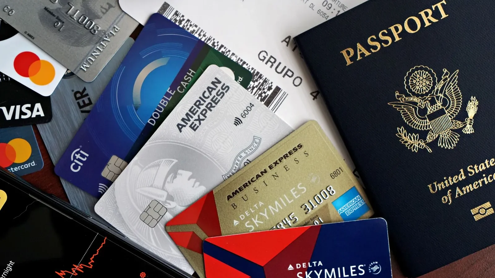 Four travel credit cards fanned out next to a passport and boarding pass on a wooden desk