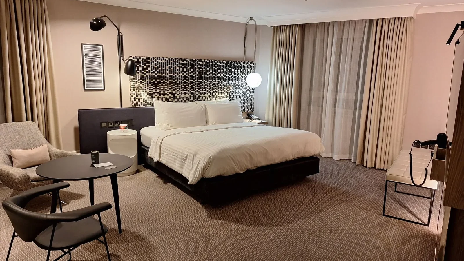 Interior of a Premier Inn hotel room showing a double bed, small desk, and compact bathroom entrance in neutral tones