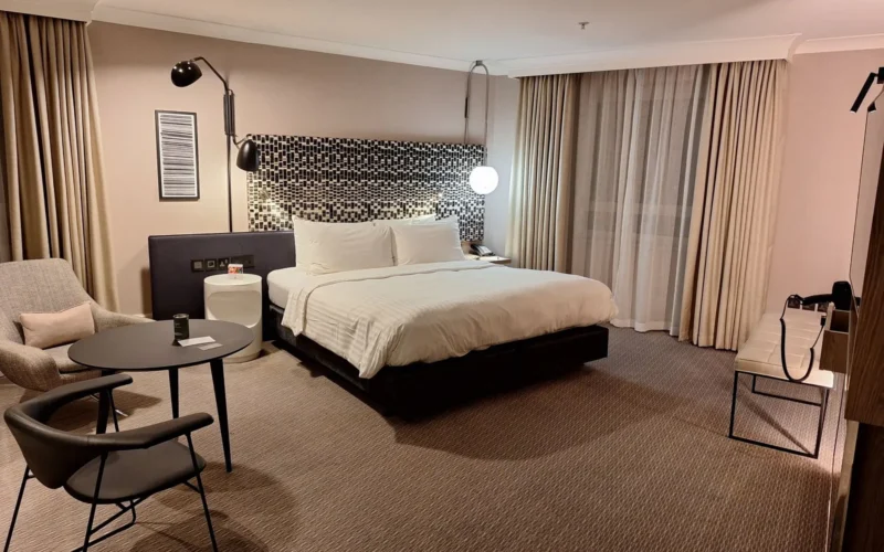 Interior of a Premier Inn hotel room showing a double bed, small desk, and compact bathroom entrance in neutral tones