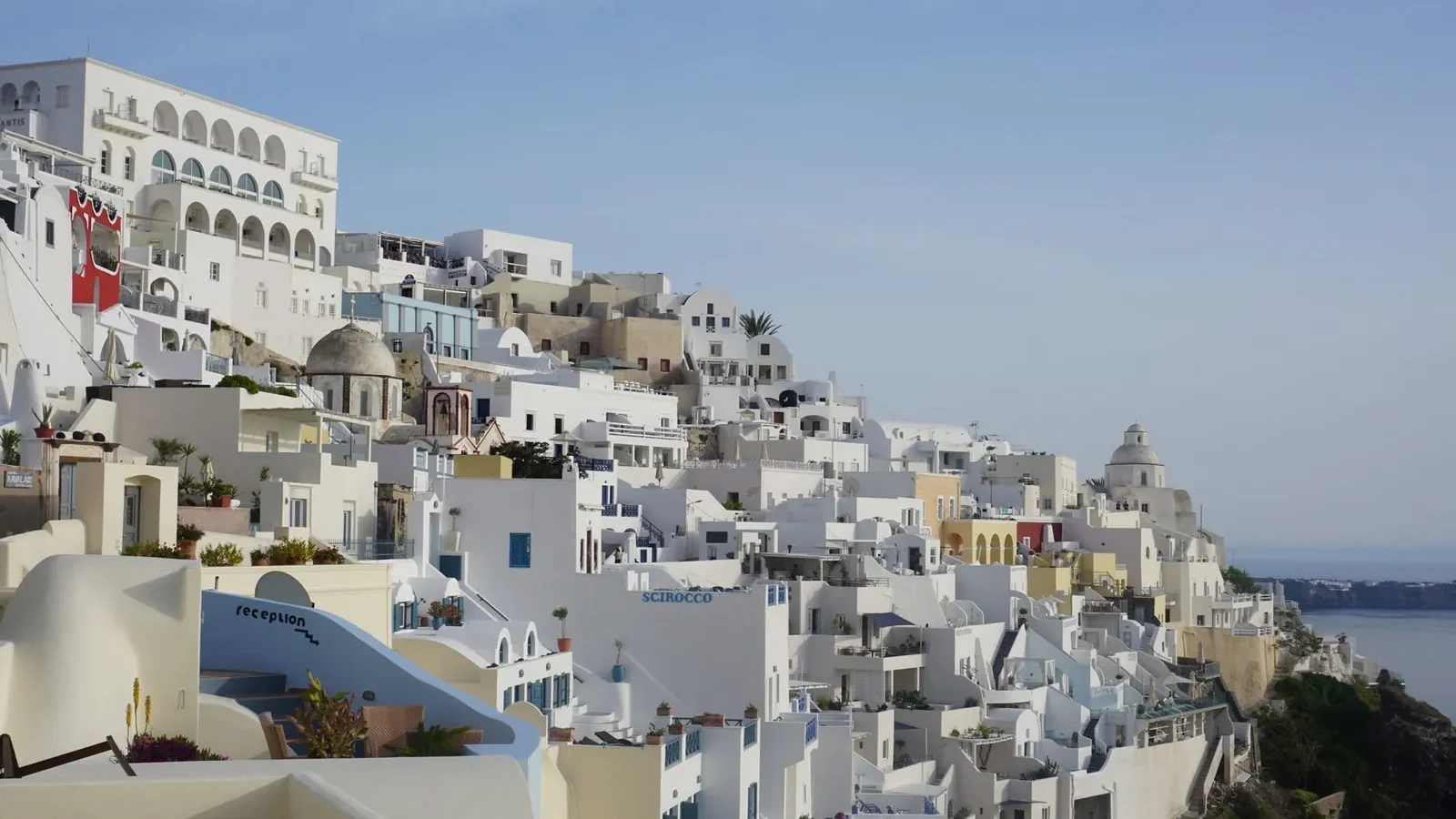 White-washed buildings and blue-domed churches on the Santorini caldera rim, viewed from Oia in morning light