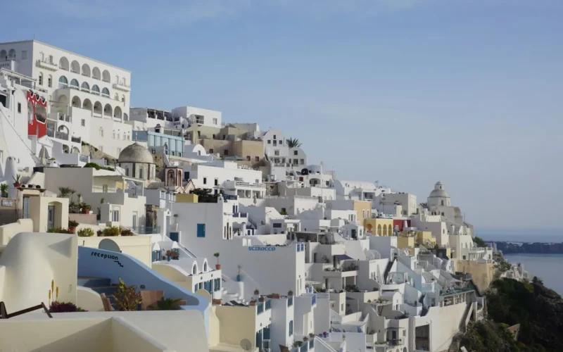 White-washed buildings and blue-domed churches on the Santorini caldera rim, viewed from Oia in morning light
