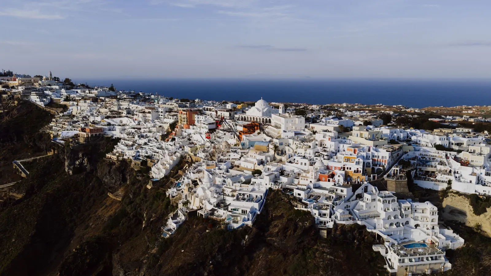 White-washed buildings and blue-domed churches on the Santorini caldera rim, viewed from Oia in morning light