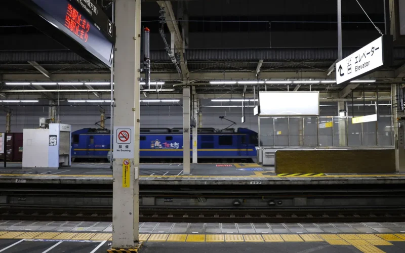 Shinkansen bullet train at a platform in Japan with a departure board overhead