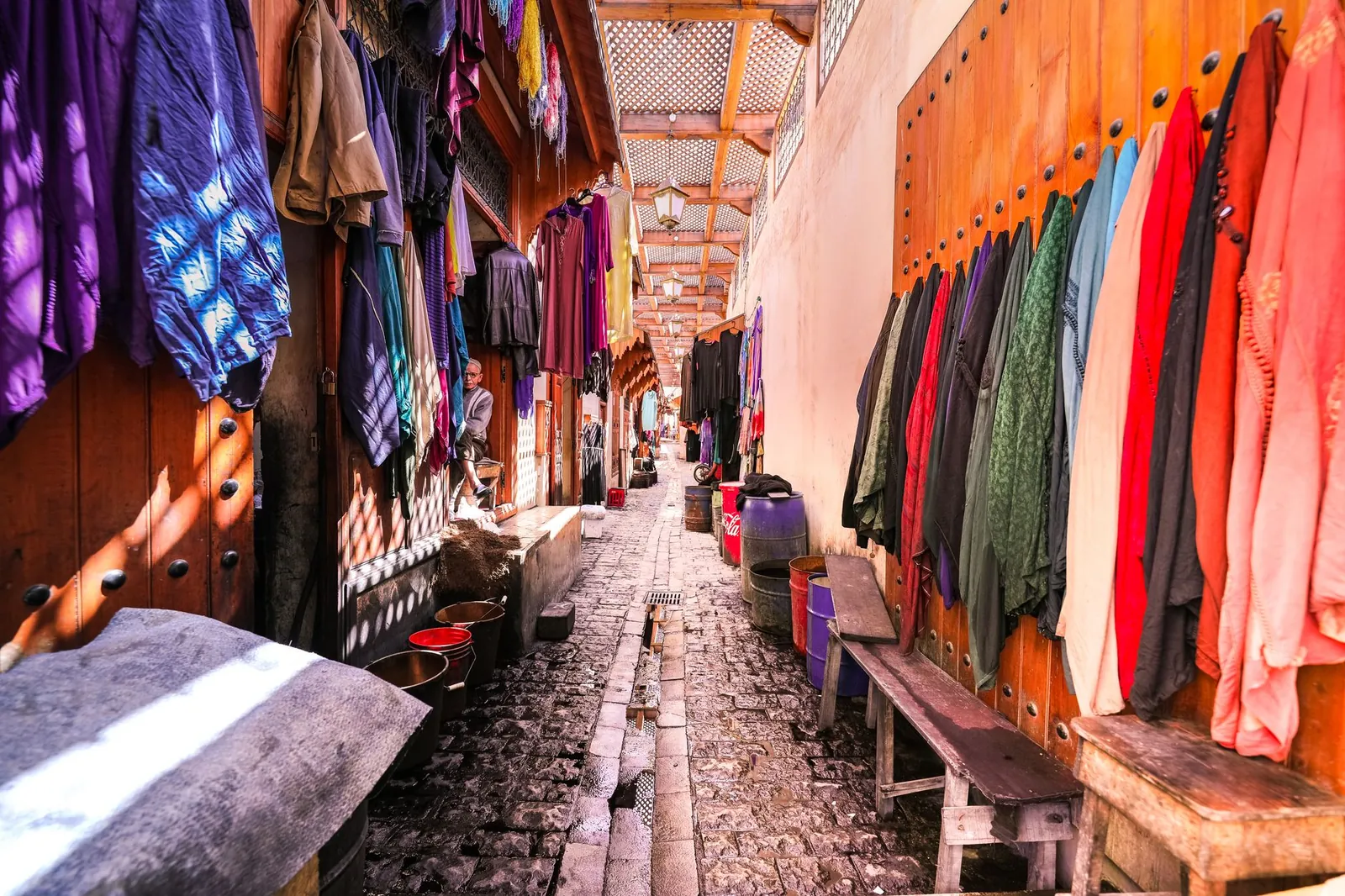 Marrakech medina alleyway with arched doorways and hanging lanterns in midday sunlight