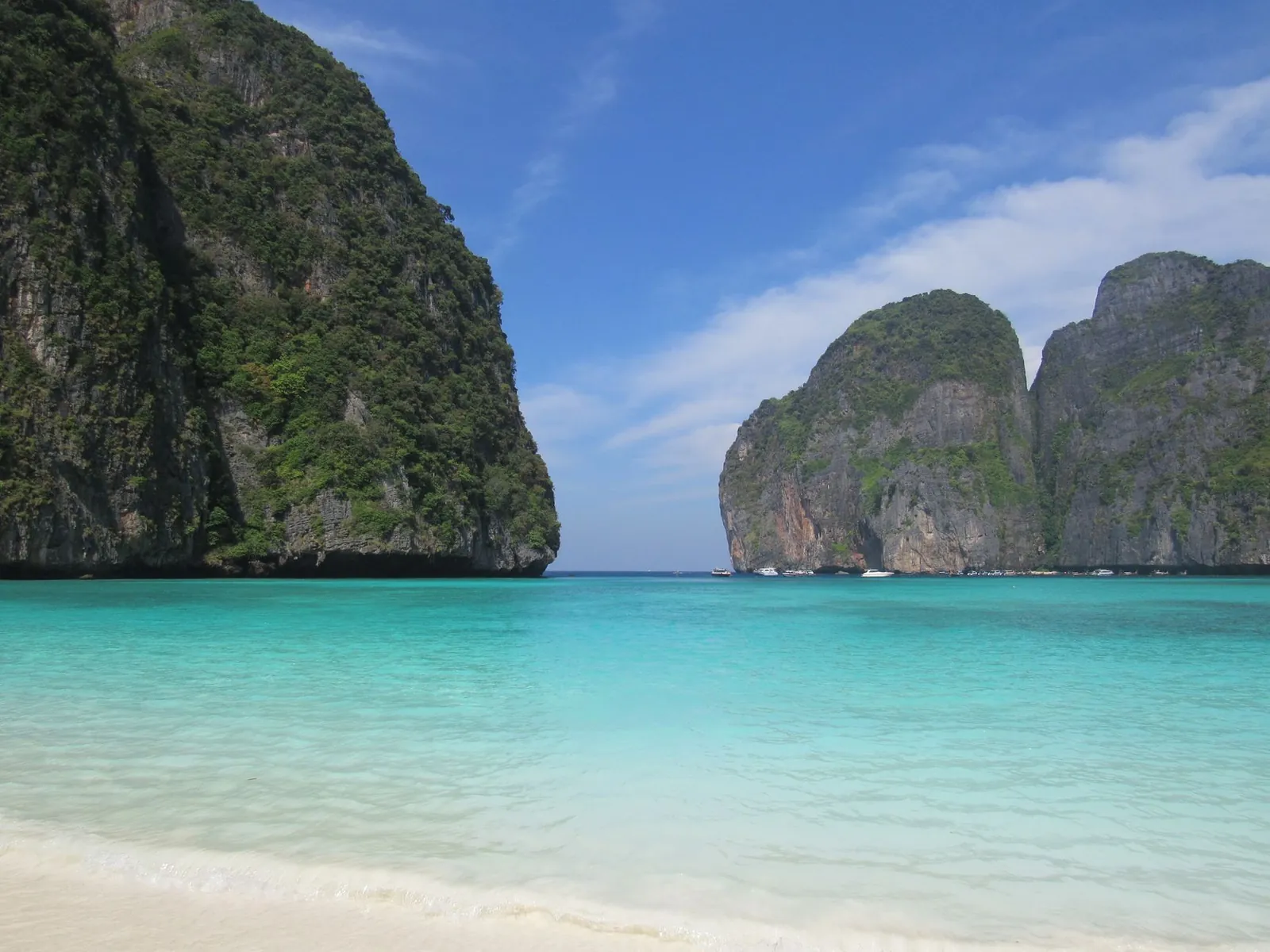 Railay Beach in Krabi surrounded by tall limestone cliffs with longtail boats on turquoise water