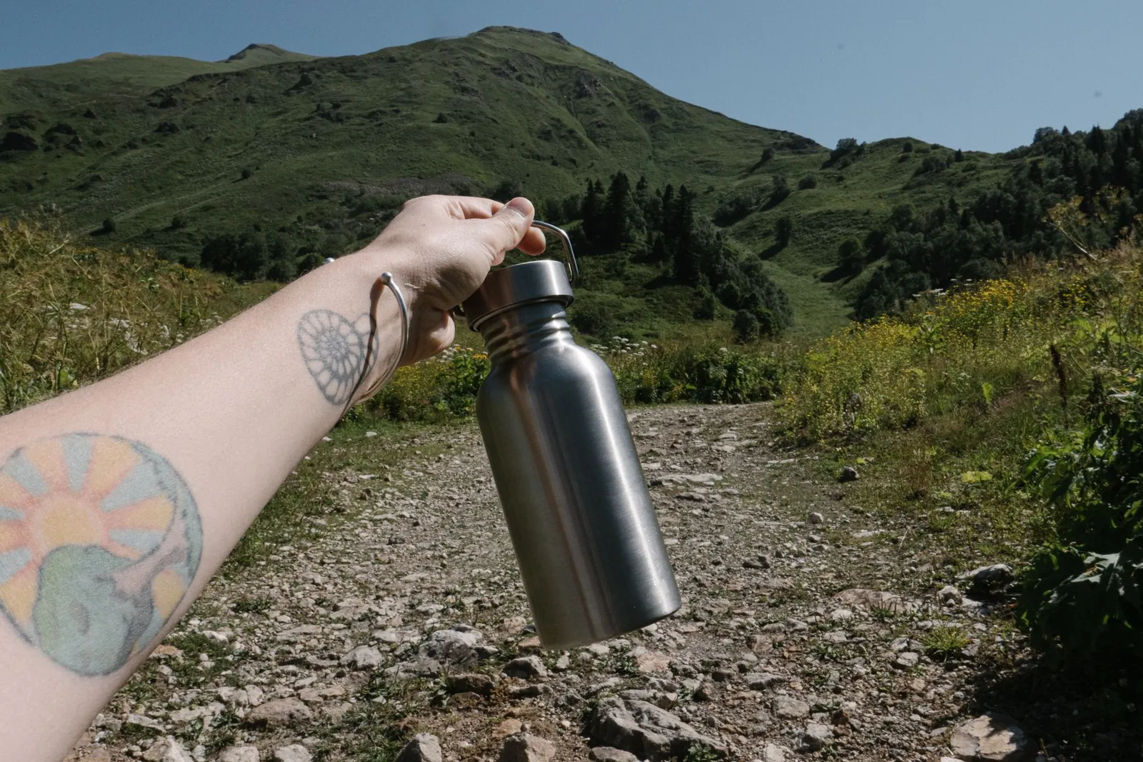 Stainless steel and recycled-plastic travel water bottles lined up against a worn hiking backpack showing size comparison